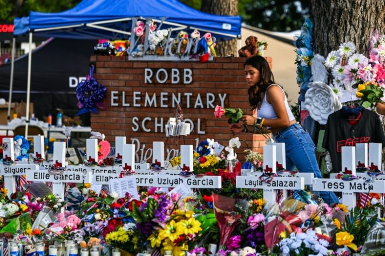 A girl lays flowers at a makeshift memorial at Robb Elementary School in Uvalde, Texas in May 2022. ©AFP