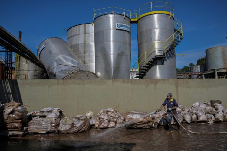 A worker uses a high pressure hose to remove mud accumulated by flooding at an industrial plant. ©AFP