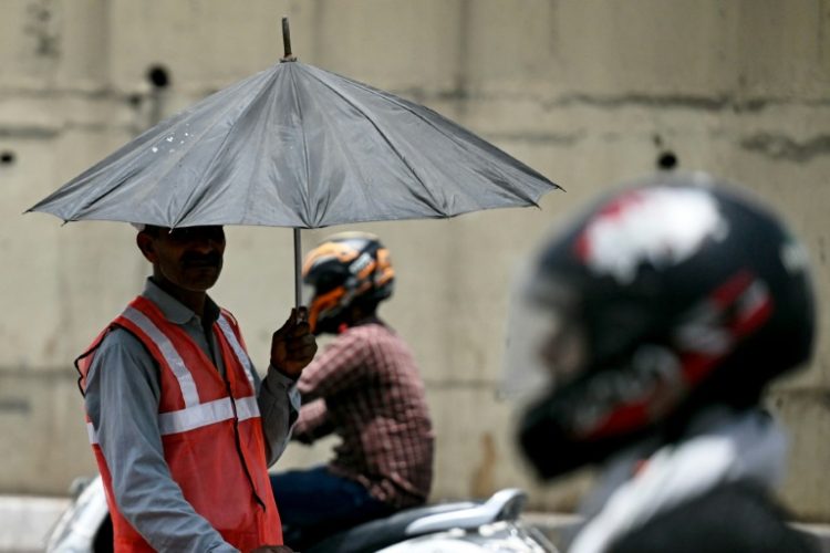 As developing countries urge increases in climate aid, a toll booth worker takes shade under an umbrella during a record heatwave in Delhi. ©AFP