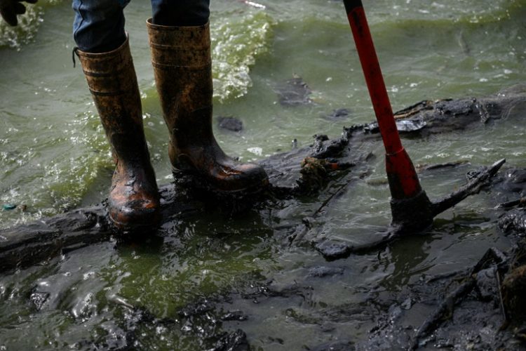 A fisherman with boots covered in oil stands on a contaminated shore of Lake Maracaibo in Venezuela, on July 11, 2024. ©AFP