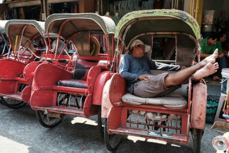 The driver of an Indonesian bechak, a traditional pedicap, sleeps in front of a market in Surakarta, Central Java. The economy of the country cooled slightly in the second quarter of 2024, according to latest data. ©AFP