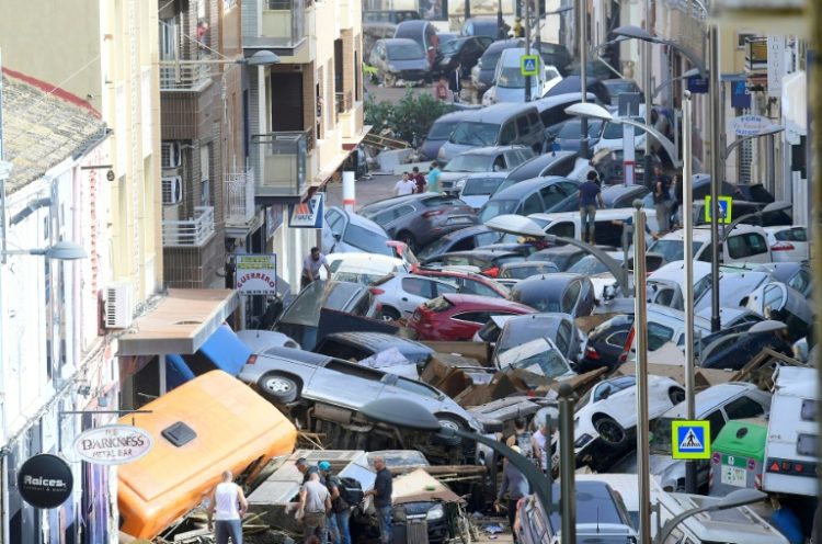 Pedestrians stand next to piled-up cars following deadly floods in Sedavi in the eastern Valencia region of Spain. ©AFP