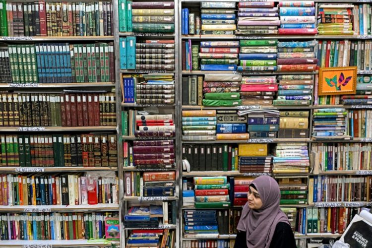 A student sits beneath packed shelves at the Hazrat Shah Waliullah public library. ©AFP