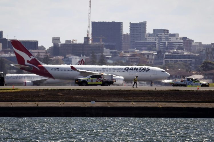 Workers check the runway as a Qantas plane prepares to take off behind them at Sydney Airport. ©AFP