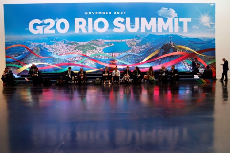 People sit and work next to a giant banner of the G20 Summit in Rio de Janeiro, Brazil, on November 18, 2024. ©AFP