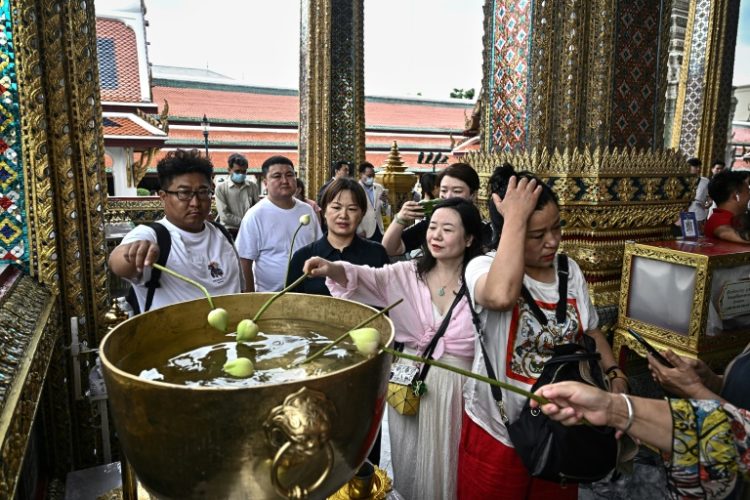 Chinese tourists dipping lotus bulbs in a water bowl, at the Grand Palace in Bangkok. ©AFP