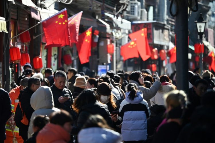 People walk below Chinese flags in an alley near a popular shopping street during the Lunar New Year holiday in Beijing. ©AFP